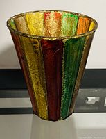 Single tapered glass vase with various vertical colored glass panels arranged in a pattern.