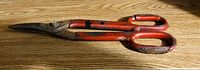 Photo of a large vintage pair of metal shears with red handles lying on a wooden surface.