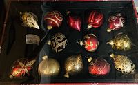 A photo of a box containing large Christmas tree ornaments in red, gold, and silver. One ornament is missing from the set.