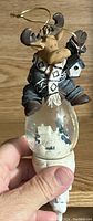 Photo of the moose snow globe tree ornament showing moose figure, scarf, birdhouse, and winter snow globe base.