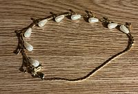 Gold-tone necklace with evenly spaced teardrop-shaped pearlescent beads, laid out on a wood surface.