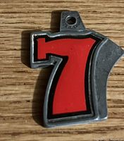 Close-up image of a pewter pendant shaped like the number 7 with red and black enamel details on a wooden surface.