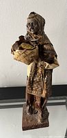 Photo of vintage paper mache figurine showing an elderly woman with shawl holding a basket on a rectangular base.