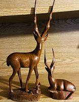 Photo showing two carved wooden antelopes, a standing mother and a reclining baby, both with detailed carved horns and smooth wooden finish.