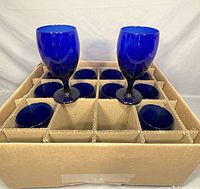 Twelve cobalt blue wine glasses arranged in a cardboard box with individual compartments to protect each glass.