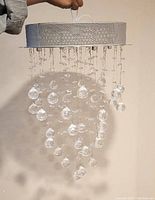 Round metal flush mount ceiling light fixture with crystal raindrop pendants hanging in a cascading design, held by hand for scale.