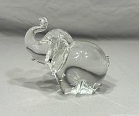 Clear glass elephant paperweight with raised trunk shown from front angle on neutral background.