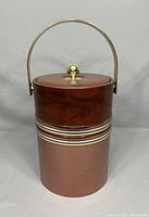 Photo shows a vinyl-covered vintage ice bucket with copper and wood grain tones, and brass handle and knob.