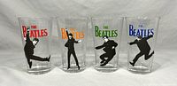 Four clear glass beer glasses with colorful 'The Beatles' text and black silhouettes of band members jumping, showing the entire set front view.
