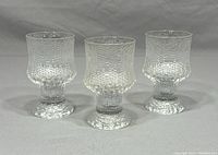 Set of three vintage Iittala Ultima Thule clear glasses with heavy textured icy pattern all over, flared base and rim, shown on neutral background.