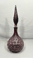 Front view of vintage Murano amethyst glass decanter with bubble texture and pointed stopper on top.