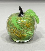 Front view of Murano glass apple paperweight showing green and gold flecked glass with green leaf and dark stem.