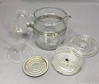 All components of the coffee percolator laid out, showing glass pot, lid, internal glass basket, stem, and metal filter plate