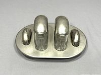Front angle view of vintage cruet set showing two glass containers with metal lids and two metal salt and pepper shakers on oval metal tray