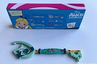 Photo of the collector key outside the box showing teal and green colors, and the themed design details including Mickey Mouse shape and Mad Hatter illustration.