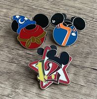 Photo showing three Disney collector pins with Mickey ears and hidden Mickey designs placed on wood surface.
