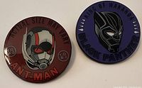 Front view of Ant-Man and Black Panther trading pins showing colored enamel designs and text.