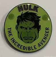 Front view of the green circular Hulk pin with text and image of Hulk's face.