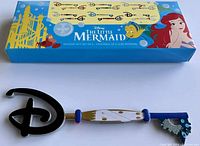 The Disney The Little Mermaid Prince Eric & Max mystery collector key outside of its packaging on a white background. The blue box with character artwork and branding is also visible.