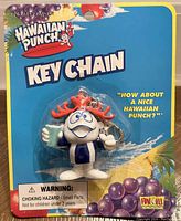 Front view of keychain featuring Hawaiian Punch HP Guy wearing a light blue and white striped shirt holding a light blue cup, attached to original blue branded backing card with warning label and tropical graphics.