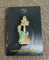 Front view of the limited edition Hard Rock 50th anniversary collector pin with gold and turquoise detail mounted on black card.
