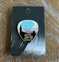 Front view of the Hard Rock guitar pick-shaped limited edition collector pin, showing detailed enamel design with diamond graphic and anniversary logos on black backing card with gold 'Limited Edition' text.