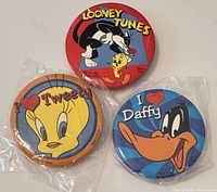Three vintage Looney Tunes button pins including a Looney Tunes logo pin, a Tweety pin, and a Daffy pin all sealed in plastic.