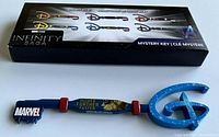 Photo shows the Marvel Studios The Infinity Saga Higher Further Faster collector key in blue with red accents and Marvel logo at one end, key shaped end at the other.