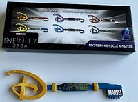 Image of the 'We Are Groot' collector key from Marvel Studios The Infinity Saga, showing the blue handle, yellow blade with Disney logo shape, and Marvel logo.