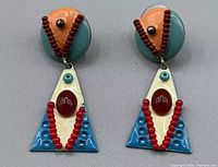 Photo of a pair of vintage boho multicolor dangle earrings showing circular teal and peach tops with dangling triangular pendants decorated with red and blue beads.