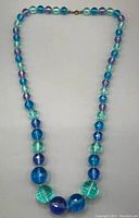 Full view of vintage chunky beaded necklace laid flat with a variety of round beads in blues and greens.
