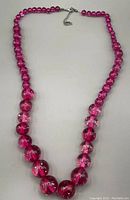 Photo showing full necklace with graduated translucent pink round beads and metal clasp with extension chain.