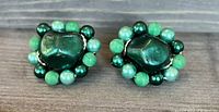 Front view of the pair of vintage Japan clip-on earrings showing emerald green faceted center beads surrounded by smaller light and dark green beads.