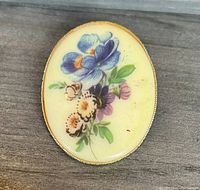 Front view of floral design brooch showing colorful flowers on cream background with gold-tone border.
