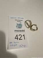 Pair of earrings displayed next to auction tag showing handwritten notes