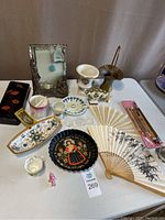 Photo of the full lot including Nippon handpainted floral tray, metal tray with painted folk art woman, fans, candlestick holder, and various small decorative porcelain and glass items.