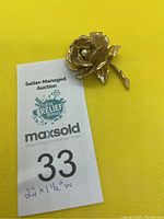 Full brooch showing gold plated textured rose with a small cultured pearl at center and stem detailed with a leaf.