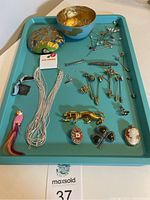 Full tray view showing all jewelry items including pins, brooches, medal, necklace, and decorative brooches arranged on turquoise tray.