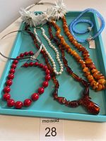 Full view of all jewelry items on blue tray including necklaces, bracelet and floral piece.