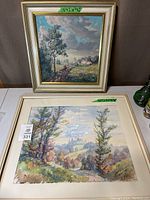 Photo showing two landscape paintings by Richard Wolf, the framed oil painting in the back and a watercolor or print in front.