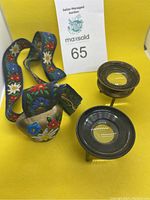 Overall view of floral ribbon holding decorative painted cowbell and two metal magnifying loupes on tripod stands