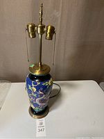 Full view of the majolica ceramic lamp with cobalt blue background, dragon and floral motifs, brass lamp hardware with two light sockets and pull chains.
