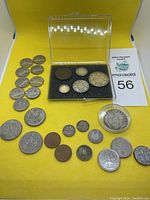 Overall lot display showing all coins including the protective casing for one coin and grouping of coins on yellow background.