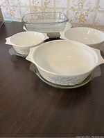 Four Pyrex Blue Iris glass baking dishes with floral pattern and handles, stacked with clear glass lids.