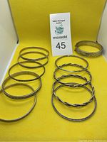 Full set of 10 silver bangles and bracelets arranged on yellow background with auction card