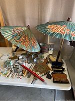 Photo of two green vintage parasols with floral designs, assorted kitchen items including cookie cutters, old tins, brass tray, and small decorative items on a table.