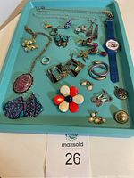 Overview photo showing vintage jewelry items including earrings, rings, chain, and a blue novelty wristwatch on a turquoise tray with lot number 26 label.