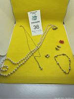 Full view of all jewelry items laid out on a yellow background including pearl necklace, 10K gold chain necklace with pearl pendant, pearl bracelet, and multiple pairs of earrings.
