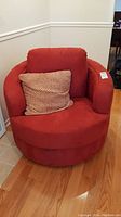 Front view of red swivel barrel chair with toss cushion placed in corner