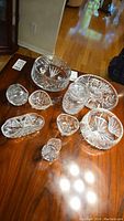 Collection of nine clear crystal dishes on wooden table, including bowls, platters, creamer, and sugar bowl, all with cut glass designs.